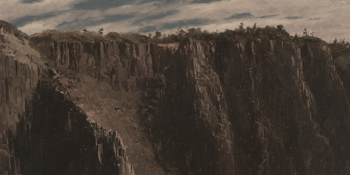 Sharp coastal cliffs above sandy beach with green vegetation on top, and bands of clouds stretching across a blue sky