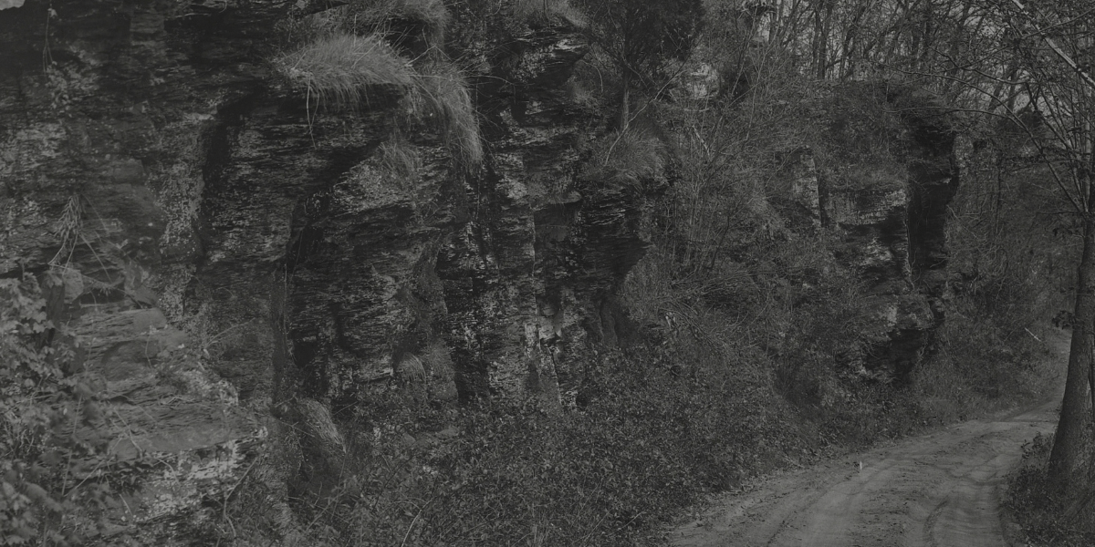 Photo of path near rocky cliffside covered by sparse trees and shrubs with bible verse Joshua 1:9 about strength and courage.